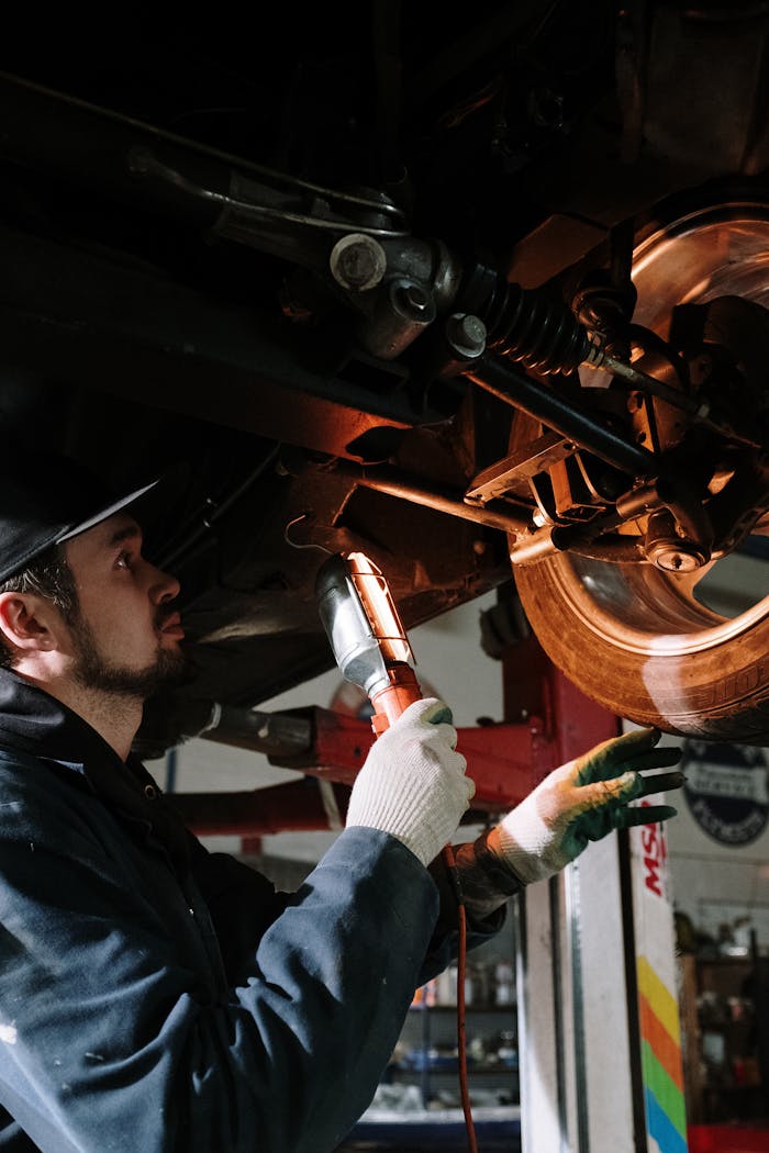 Mechanic uses a flashlight to inspect cars suspension in a garage setting.